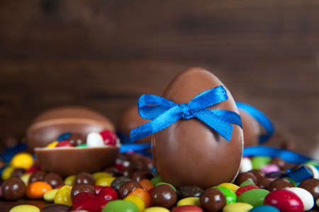 Happy Easter greeting card with delicious sweets, chocolate eggs and blue bow on wooden background, space for text.の写真素材