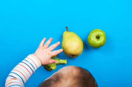 Child reaches out with his hand for pear and apple on blue background. Baby food, first feeding. .の写真素材