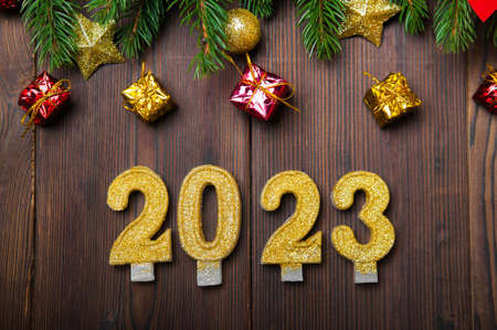 Happy New Year 2023 greeting card. Candle numbers on wooden background and layout of Christmas tree, balls, gifts. Close up and copy space, selective focus.の写真素材