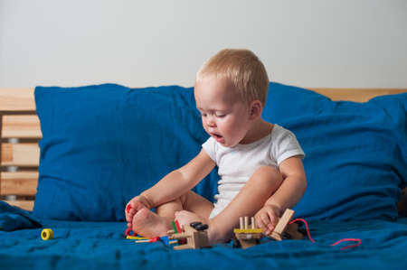 Toddler boy plays with wooden constructor train on bed close-up..の写真素材
