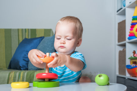 Handsome toddler boy playing with educational wooden and plastic toys in children's room.の写真素材