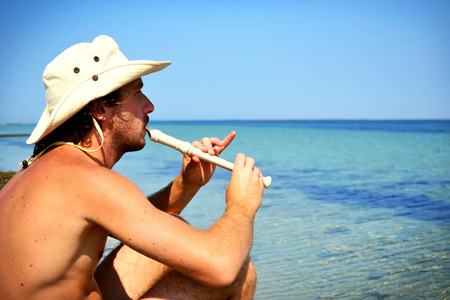 Young man playng flute near the seaの写真素材
