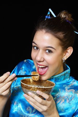 A young girl in oriental dress, eating a spare rib with chopsticks.の写真素材