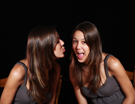 Twin sisters. One sister pretends to gag at her twin's show of affection.  Double exposure.の写真素材
