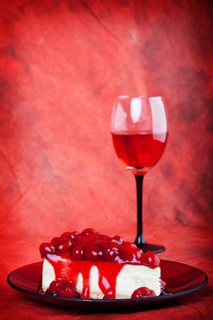 Decadent cherry cheesecake served on a candy apple red plate with red wine,on a red background.の写真素材