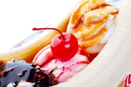 A closeup view of a delectable banana split, with chocolate, strawberry, and caramel drizzled on mounds of vanilla ice cream and topped with a red cherry.  Shot on white background.  Selective focus on cherry.の写真素材