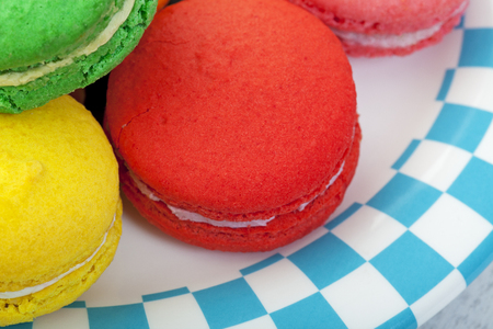 Closeup of brightly colored macaroon cookies on a plate edged in a blue and white checker.の写真素材