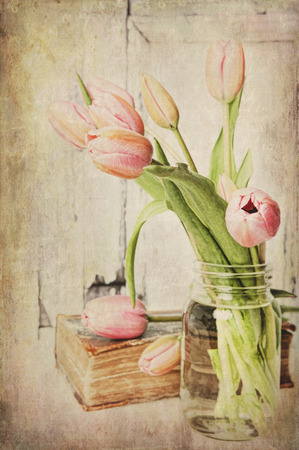Fine art image of pink tulips in a jar next to a vintage book. Textured.の写真素材