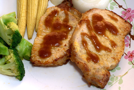 The close up shot for two pieces of the pork steak topped with the brown sauce served with many kinds of vegetables.の写真素材
