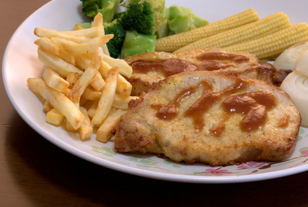 The close up shot for the pork steak topped with the brown sauce served with french fried and many kinds of vegetables.の写真素材