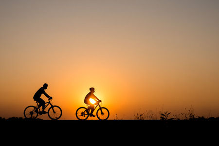 Silhouette of cyclist with friend in motion on the background of beautiful sunsetの写真素材