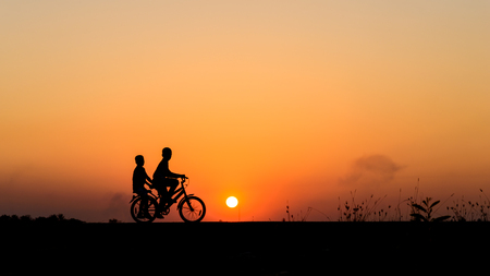 Silhouette of cyclist with friend in motion on the background of beautiful sunsetの写真素材