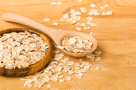Rolled oats (oat flakes) in a wooden spoon and cup on a wooden background. Close-up.
