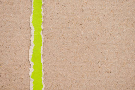 Teared, ripped green paper on brown backgroundの写真素材
