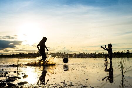 Silhouette of boy playing football in water at countryside in thailandの写真素材
