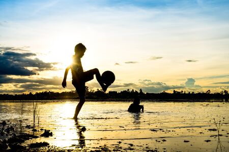 Silhouette of boy playing football in water at countryside in thailandの写真素材