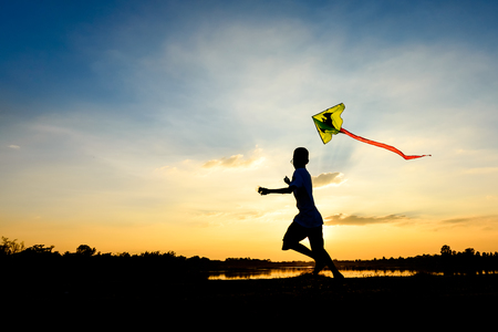 silhouette of children flying a kite at sunset invoke childhood memoriesの写真素材
