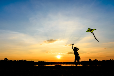 silhouette of children flying a kite at sunset invoke childhood memoriesの写真素材