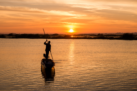 silhouette of fisherman on long tail boat in the lake in morning, Thailandの写真素材