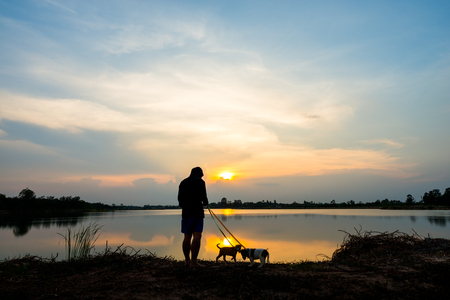silhouette portrait of a man and his puppy on a stunning sunset.の写真素材