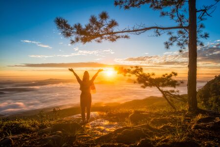 Young woman standing and hands up on top of mountain in morning winter watching the sunrise, travel and freedom conceptの写真素材