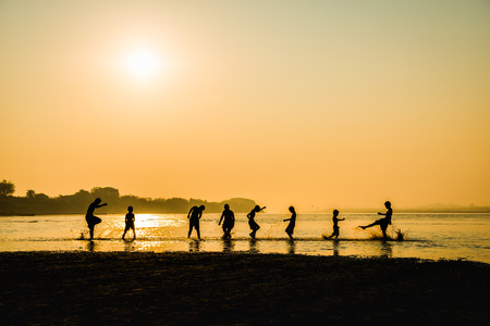 Silhouette of children playing water with friend in river on sunrise backgroundの写真素材