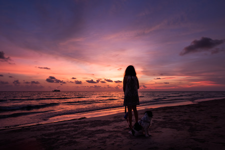 Silhouette of Asian girl with dog on the beach on sunset backgroundの写真素材