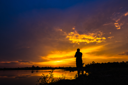 Silhouette photographer at the lake on sunset background to enjoy colorful sunset skyの写真素材