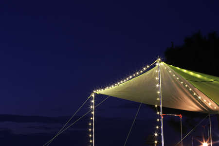Green roof tent lit at night with blue sky backgroundの写真素材