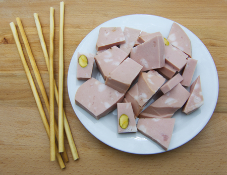 Mortadella Bolognese cut into cubes on a plate, with bread sticks, wooden tableの写真素材