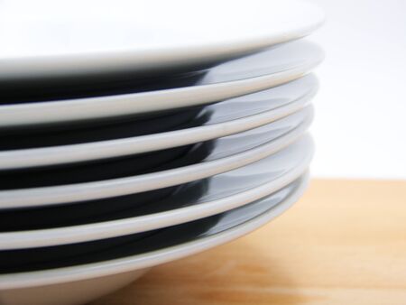 Close-up of stack of white plates on wooden table, white background