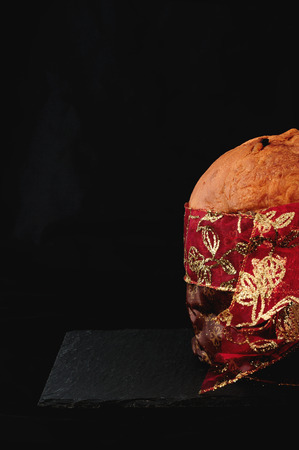 Christmas essence, panettone with red ribbon on black background, vertical. Panettone is a typical Christmas cake in Italyの写真素材