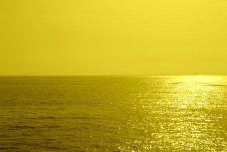 Summer minimalist background, yellow monochromatic glittering sunset on the sea, with the sun coming down to the horizonの写真素材