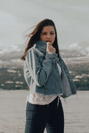 portrait of a beautiful young girl with blue jacket touching his hair at sunriseの写真素材