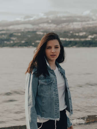 portrait of a beautiful young girl with blue jacket touching his hair at sunriseの写真素材