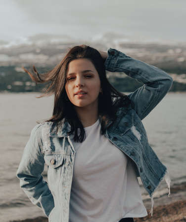 portrait of a beautiful young girl with blue jacket touching his hair at sunriseの写真素材