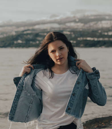 portrait of a beautiful young girl with blue jacket touching his hair at sunriseの写真素材
