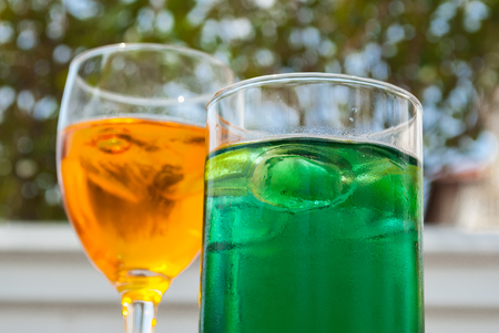 two cocktails colored green and orange served on the terraceの写真素材