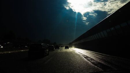 ray of sunshine breaks through a cloud and illuminates the wet roadの写真素材