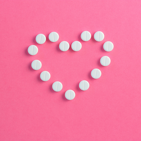 Heart shaped of white pills on pink backgroundの写真素材