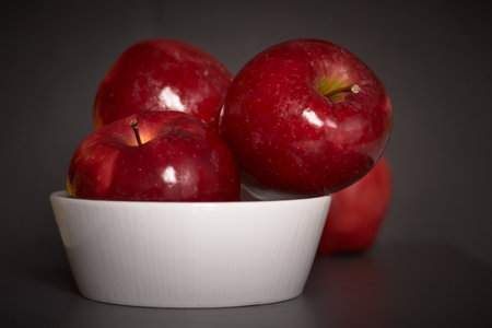 Several bright red apples put in a white ceramic bowl with a dark background.の写真素材