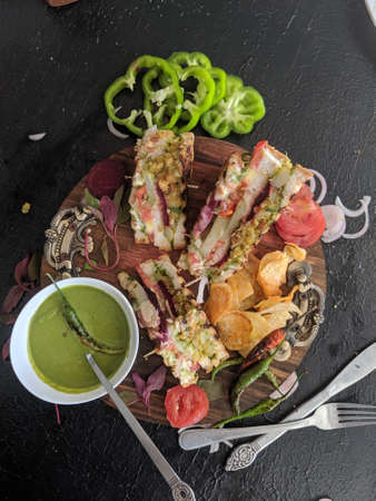 Messy Bombay masala sandwich with beetroot, potato and vegetable filling, with a green chili mint coriander dip and chips, served on a wood platter, Indian messy sandwich, spicy food.の写真素材