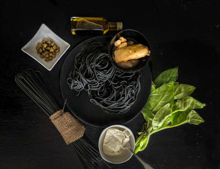 Cooked black squid ink pasta, ingredients to make a pasta dish, spinach, smoked salmon, fresh cream cheese, capers and olive oil on a black background, Italian cuisineの写真素材