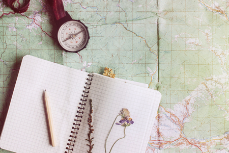 wanderlust and adventure concept, compass and notebook with wildflowers and pencil on map, top view, vintage toned image, space for textの写真素材