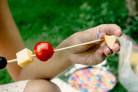 woman making appetizers putting cheese olives tomatos on wooden stick, picnic kitchen outdoors, catering buffet at summer celebrationの写真素材