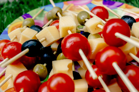cherry tomatoes olives cheese on wooden stick appetizer, picnic outdoors, catering buffet at summer celebrationの写真素材