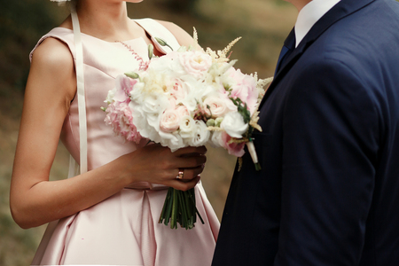luxury bride and groom holding hands and gorgeous pink and white bouquet, rich wedding couple, tender romantic moment at garden with blossomsの写真素材