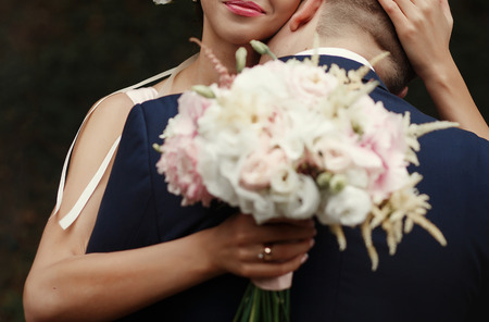 groom kissing bride at neck, luxury wedding couple hugging, tender romantic moment at garden with pink blossomsの写真素材