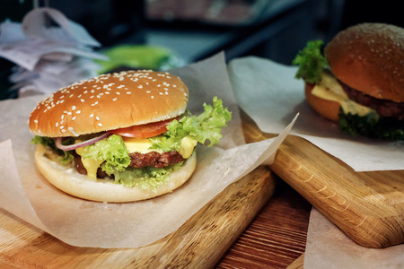yummy burger. serving cheeseburger or hamburger with salad and tomatoes onion and cheese on wooden desk. catering in food court at mall concept. space for textの写真素材