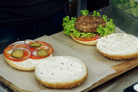 process of making burger. cooking hamburgers and cheeseburgers, putting ingridients on wooden desk. catering in food court at mall concept. space for textの写真素材